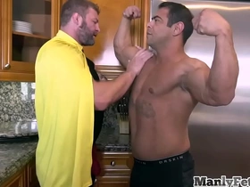 Muscle-bound superhero bends over his partner, revealing his tattooed back and bare ass. His jock uniform adds a kinky twist to their anal encounter in the kitchen.